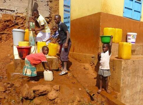 Man with children fetching water from a communal spring with a basin